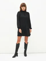 Vestido corto negro con cuello alto, mangas largas abullonadas y falda escalonada.