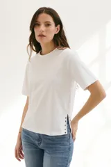 Remera blanca de algodón de corte recto, con cuello redondo y mangas cortas. Presenta detalle de aberturas laterales con ojales metálicos.