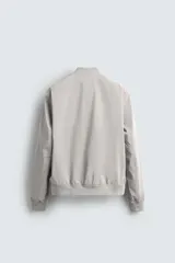 Cazadora bomber ligera gris confeccionada en tejido técnico. Cuello y puños en rib elástico, manga larga, bolsillos de vivo en cadera y bolsillo interior. Cierre frontal con cremallera.