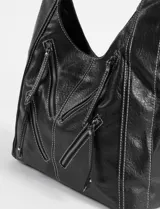 Cartera hobo color crudo de cuero sintético, con correa de hombro ajustable y múltiples cierres decorativos en el frente.