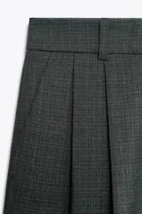 Pantalón gris de tiro alto con pinzas delanteras, bolsillos frontales y pernera ancha. Cierre frontal con cremallera, botón interior y gancho.