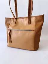 Bolso tipo tote de cuero color camel con paneles laterales texturizados. Tiene doble asa de hombro, cierre superior con cremallera y bolsillos internos.