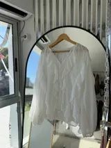 Blusa blanca traslúcida con escote en V y volantes en el frente y las mangas.