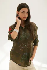 Camisa beige de manga larga con cuello clásico y cierre frontal con botones. Presenta bordados con motivos florales y geométricos en tonos azules, rojos y verdes.