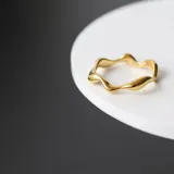 Anillo dorado de acero quirúrgico con forma irregular simulando el movimiento de una ola.