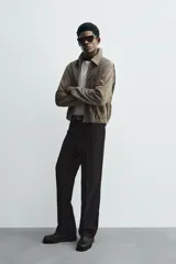 Cazadora de hombre color verde oliva, confeccionada en piel con acabado ante. Presenta un corte boxy fit, cuello solapa, cierre frontal de cremallera, bolsillos delanteros y elásticos en puños y bajo.