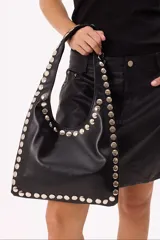 Cartera estilo hobo negra de cuero sintético con tachas metálicas plateadas en el borde.