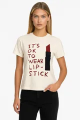Remera de algodón color crudo con estampado de un labial rojo y texto en color bordó que dice "It's OK to wear lipstick". Corte clásico, cuello redondo y mangas cortas.