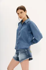 Camisa celeste de tencel con calce recto, manga larga amplia con frunces en los hombros y cuello camisero. Mangas terminadas en puño con botón y ojal. Cartera delantera con botones metálicos con el logo de la marca.