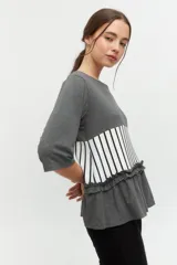 Remera gris con mangas 3/4, corte recto y detalle de volados en el ruedo. Presenta una franja horizontal con estampado de rayas verticales blancas y negras.