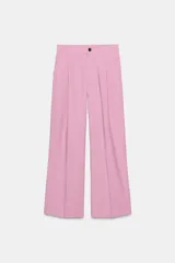 Pantalón de vestir color rosado, de tiro alto y corte ancho. Presenta bolsillos laterales y pliegues frontales. Cierre frontal con cremallera y botón.