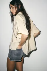 Shorts de jean de algodón, tiro alto, color azul claro desgastado. Presenta cinco bolsillos, cierre frontal con botón metálico y bajo desflecado con vuelta.