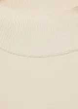 Jersey color crudo de punto fino con cuello perkins, manga larga y detalle de botones metálicos en el hombro. Corte recto.