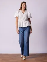 Blusa blanca de algodón con bordado broderie, escote en V con abertura central y botones, cintura elastizada y mangas cortas con terminación elastizada.