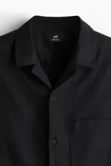 Camisa negra de manga corta en mezcla de algodón y lino. Modelo con cuello abierto, tapeta lisa y bolsillo superior abierto.