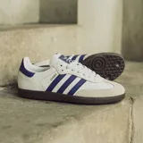 Zapatillas deportivas de cuero blanco con detalles en azul y suela de goma, modelo clásico de adidas.