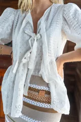 Camisa blanca con bordado calado, escote en V con lazos y mangas abullonadas. Confeccionada en tela suave y liviana.