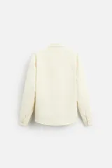 Sobrecamisa negra de tejido con elasticidad, cuello solapa y manga larga acabada en puño con botón a presión. Tiene bolsillos de plastrón en el pecho y cierre frontal con botones a presión.