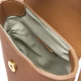 Bandolera pequeña color marrón habano, con solapa frontal que se cierra con broche metálico dorado. El cuerpo del bolso tiene textura de tejido. Incluye ranuras internas para tarjetas y correa larga regulable y desmontable.