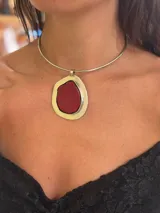 Collar tipo choker rígido de metal plateado, con un dije colgante de forma orgánica que contiene una piedra roja texturizada engarzada en un marco metálico plateado.