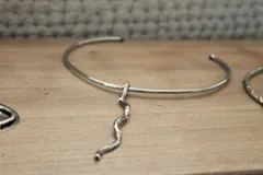 Gargantilla rígida plateada con dije colgante en forma de rama. Hecha a mano en alpaca.