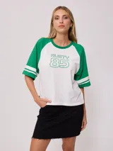 Remera bicolor blanca con mangas cortas raglán verdes con dos rayas blancas en los puños. Estampado frontal con el logo de Rusty y el número 85 en verde.