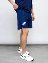 Short deportivo azul con escudo del Club Nacional de Football en la pierna derecha y detalles tricolor.