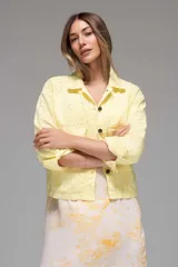 Campera de jean liviano color amarillo pálido, con cuello camisero, cierre frontal con botones y mangas largas con puños abotonados. Presenta bolsillos de parche en el pecho y detalle de broderie calado en forma de flores.