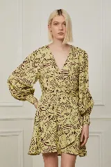 Vestido corto color amarillo con estampado abstracto en marrón, escote en V cruzado, mangas largas abullonadas con puños elásticos y falda con volantes.
