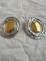 Par de aros grandes ovalados plateados con centro dorado y diseño irregular.