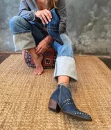 Botín de cuero azul con tachas doradas, cierre lateral y taco de madera.