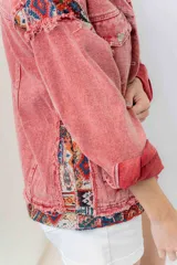 Campera de jean oversize, color rojo desgastado, con aplicaciones de tapicería multicolor de estilo étnico en hombros y ruedo, y terminaciones desflecadas.