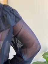 Blusa de gasa azul marino traslúcida con volados en los hombros y mangas largas abullonadas.
