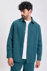 Camisa de manga larga color verde azulado, con cuello camisero, botones frontales y dos bolsillos de parche con tapa en el pecho.