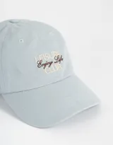 Gorra marrón de gabardina con efecto lavado y bordado frontal con la frase "Leisure Enjoy Life Club" en color blanco.