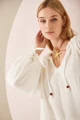 Camisa oversize blanca de lino, con cuello en V, mangas largas abullonadas con puños elásticos y lazos decorativos.