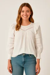 Blusa blanca de algodón con escote redondo, mangas largas abullonadas con puños elásticos y detalles de encaje calado en el frente y las mangas.