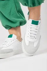 Zapatilla de cuero blanco con detalles en verde, diseñada para conjuntos casuales y estilo atemporal.