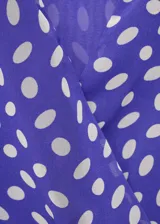 Vestido corto de poliéster, color azul con estampado de lunares blancos. Presenta cuello pico cruzado, tirantes anchos y diseño evasé con cierre lazo cruzado en la cintura.