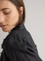 Camisa blanca de lino con cuello clásico, abotonada al frente con botones de madera, mangas largas con volados en los hombros y corte femenino.