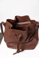 Cartera tipo botellero de cuero negro con efecto trenzado, tamaño mediano, cierre con frunce, correa ajustable con hebillas para usar al hombro o cruzada, doble bolsillo interior (uno con cierre) y forro de algodón.