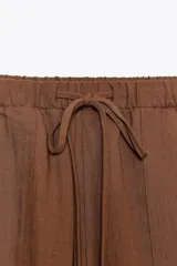 Pantalón jogger color gris claro, de tiro alto con cintura elástica ajustable con cordones, bolsillos delanteros y traseros con solapa, y puños elásticos en el bajo.