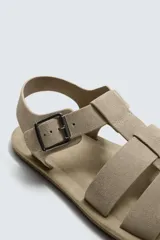 Sandalia tipo cangrejera color beige, con tiras de cuero serraje y hebilla lateral ajustable.