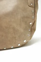Cartera tipo hobo color beige con tachas plateadas en el borde inferior y asa de hombro trenzada.