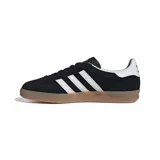 Zapatillas Adidas Gazelle Indoor negras con las tres tiras laterales blancas, detalle dorado con el nombre del modelo y suela de goma color caramelo.