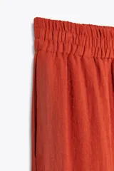 Pantalón marrón de tiro alto con cintura elástica, bolsillos delanteros y pernera ancha.