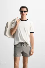 Short de baño con textura seersucker a rayas verticales azul marino y blanco. Tiene cintura elástica ajustable con cordón, bolsillos frontales y traseros, aberturas laterales en el bajo y forro interior.