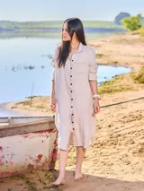 Vestido camisero largo de lino color beige, con cuello clásico, manga larga con puños abotonados y cierre frontal con botones. Tiene un bolsillo de parche en el pecho.