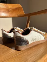 Championes urbanos de cuero color blanco hueso con detalles en marrón. Presentan cordones de algodón color crudo y logo bordado en el lateral.