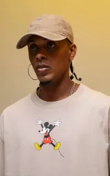 Remera color beige de manga corta con cuello redondo y calce oversize. Estampado en la espalda con diseño de Mickey Mouse con auriculares y elementos de audio.